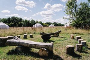 A campsite with circular arrangement of yurts and wood benches surrounded by trees in a natural setting