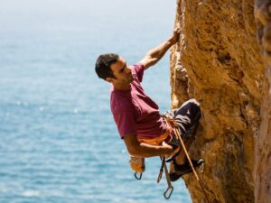 A determined man scales the towering red rocks with the vast blue sea as his backdrop