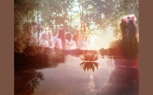 A serene and dreamy landscape, featuring a tranquil lake with a beautiful lotus flower in the center. Surrounding the lake, a group of women are joyfully celebrating and connecting with nature