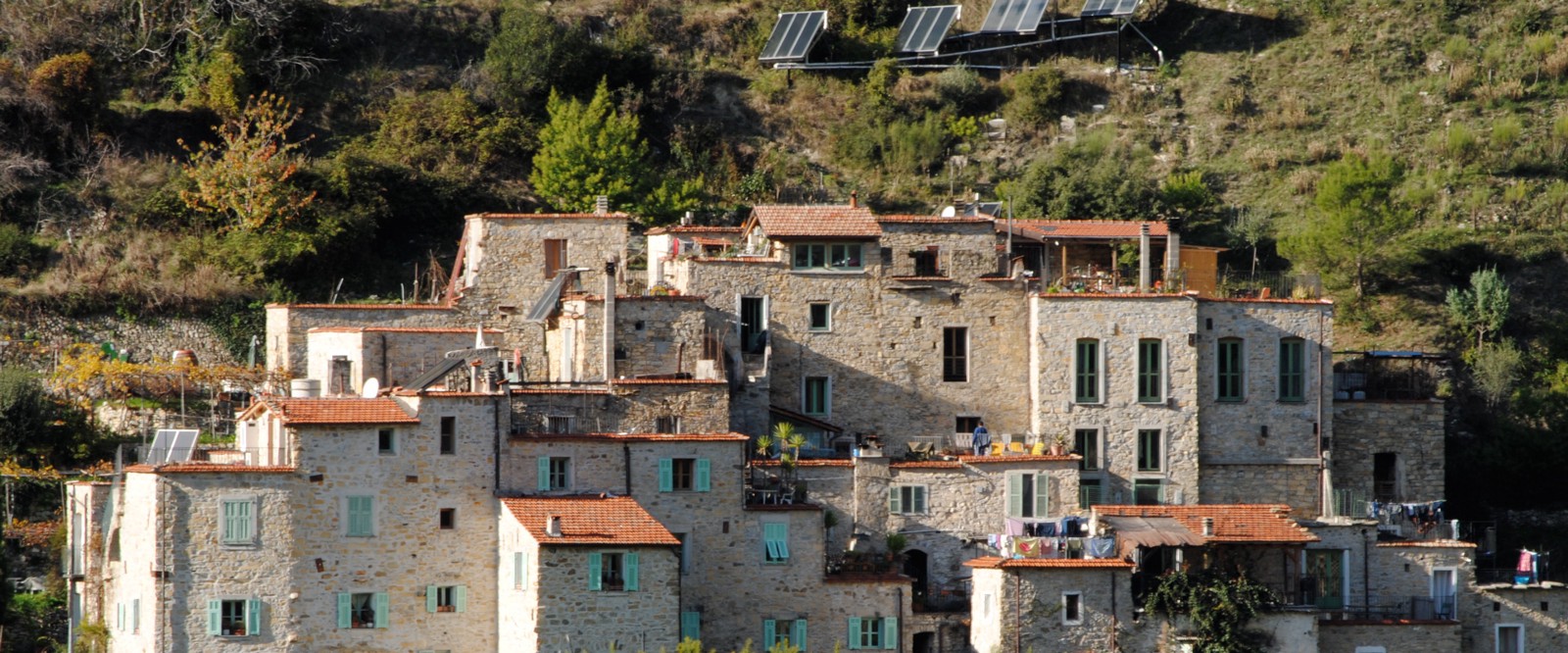 A view of the Ecovillage Torri Superiore in Italy, featuring a cluster of eco-friendly homes surrounded by rolling hills and forests