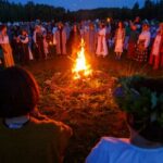 A group of people, adorned with traditional laurel wreaths, gather around a warm fire to celebrate the solstice.