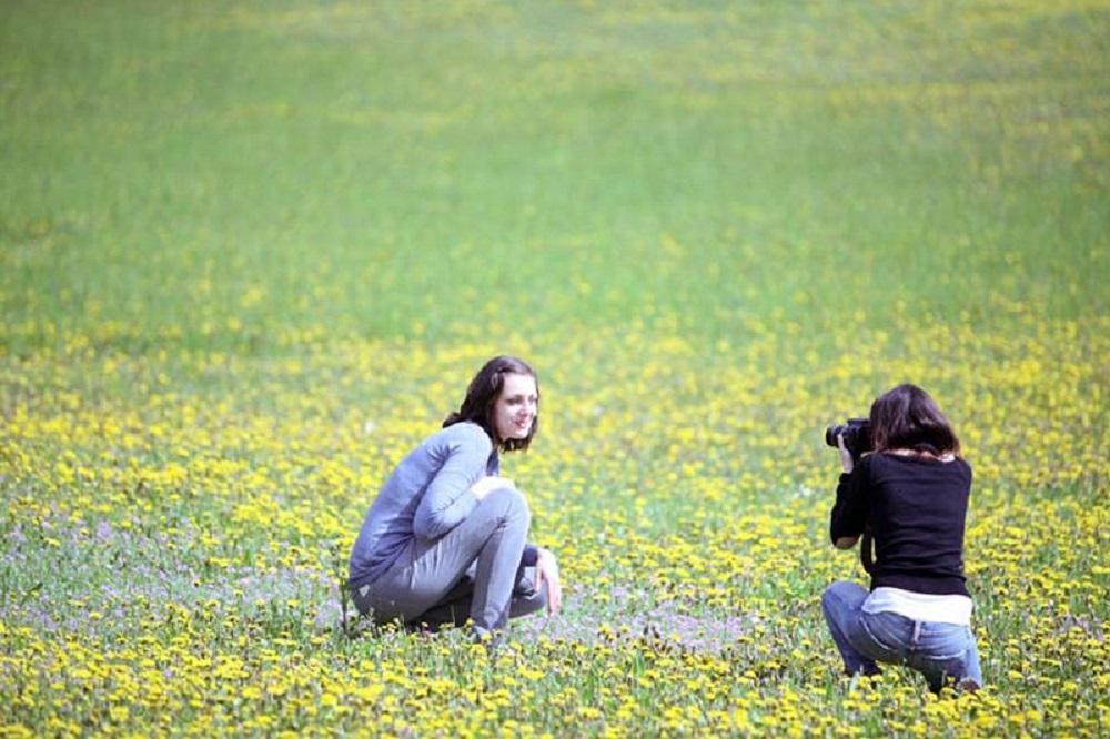 A woman taking a photograph of another woman surrounded by flowers in a field in Tuscany, Ital